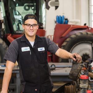 A student poses in front of a tractor inside Moorhead's Diesel Equipment Technology lab